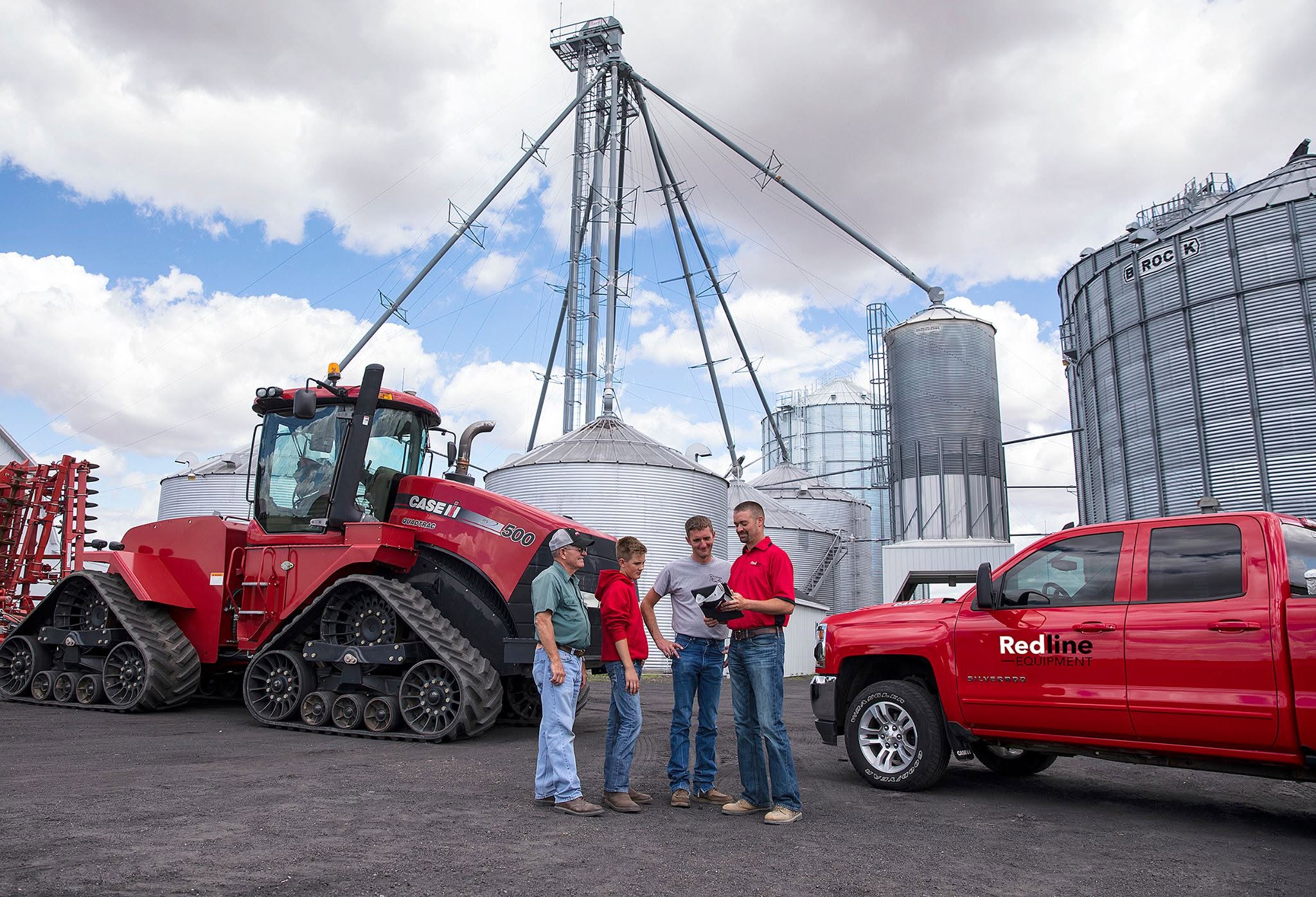 A Redline team member reviews a tablet with three generations of a farm family beside a Case IH Steiger 500 Quadtrac and grain bins